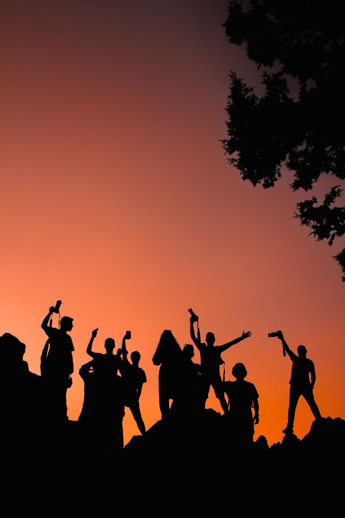 A group of people celebrating joyfully with raised arms at sunset in Aladağ, Türkiye, captured in silhouette.
